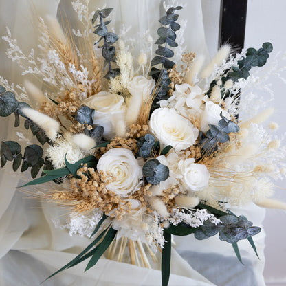 A bridal bouquet featuring preserved ivory roses, eucalyptus, bunny tails, and other white floral elements with green foliage.