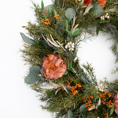 Decorative wreath with greenery, orange flowers, and berries on a white background